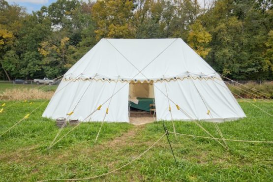 large round ended white canvas tent in a field with trees behind