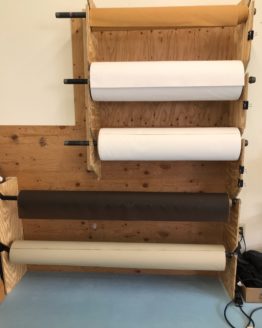 Five oilskin rolls in different colors and sizes. They are hanging on a wooden rack in a horizontal position and separated by a short length.