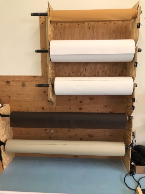 Five oilskin rolls in different colors and sizes. They are hanging on a wooden rack in a horizontal position and separated by a short length.