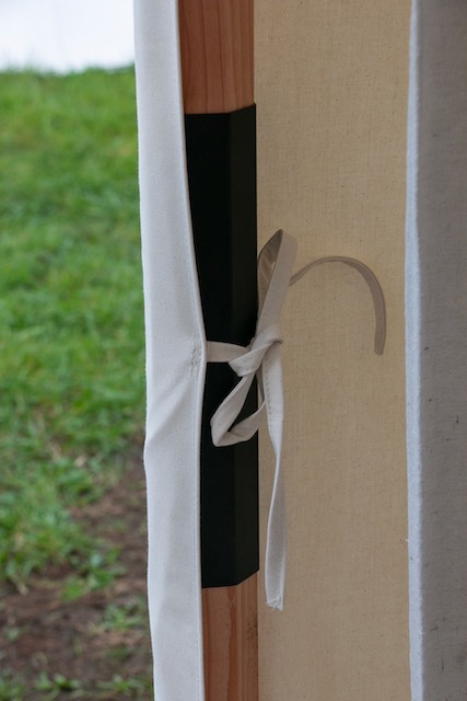 A wooden pole with a black pole sleeve and a tent's white fastening string tied around it in a secure knot.