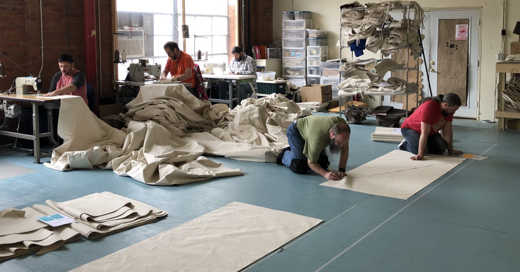 Tentsmiths is Hiring Tentsmiths sewing workshop with people sewing, measuring, and cutting