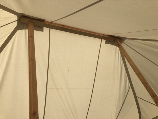 inside a white canvas tent looking up at wooden poles