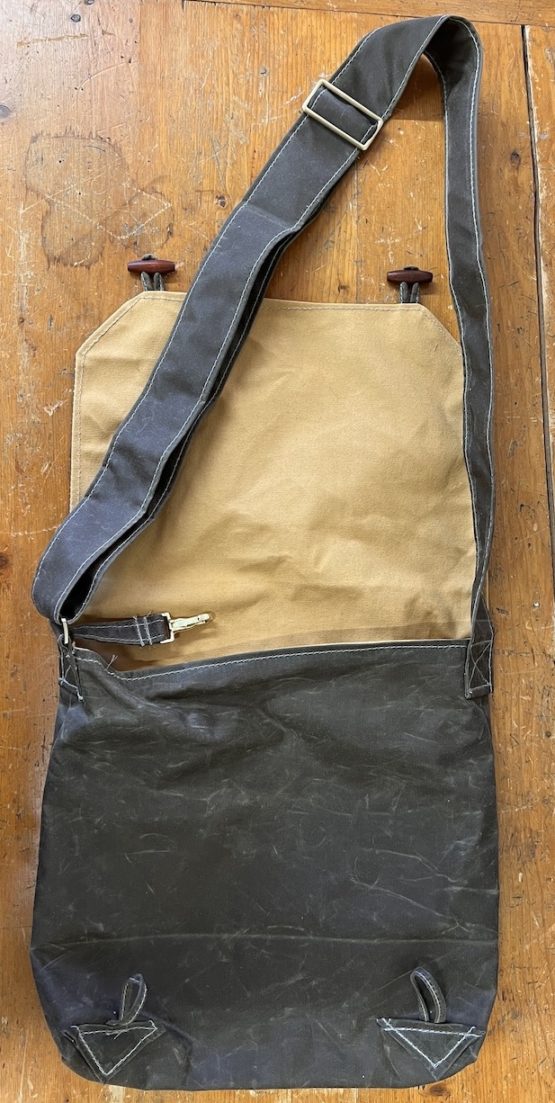 A black satchel bag opened and laid flat on a wooden surface with the shoulder strap stretched above it.