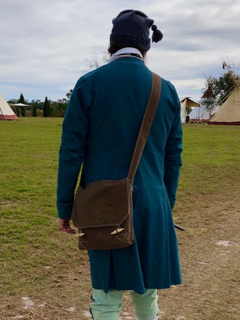 Man dressed in 18th Century clothes from the back with a dark oilskin shoulder bag