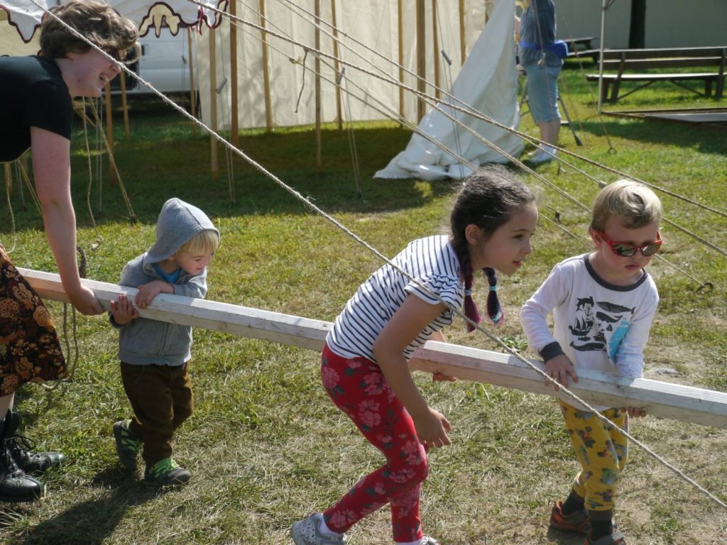 person and three children carying wooden pole