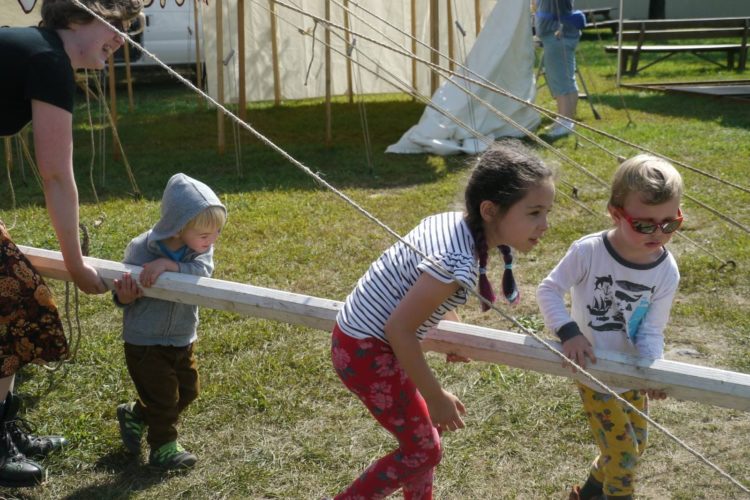 person and three children carying wooden pole