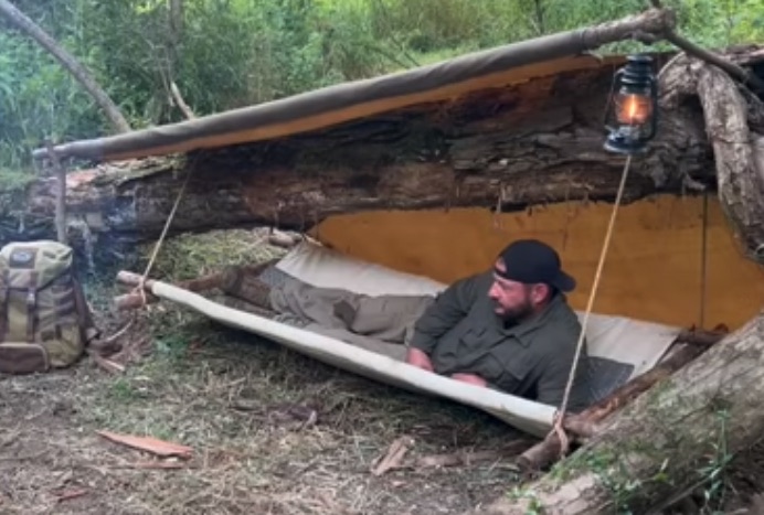 white male laying in shelter in woods